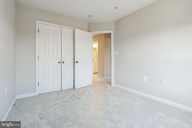 unfurnished bedroom featuring baseboards, a closet, and light carpet