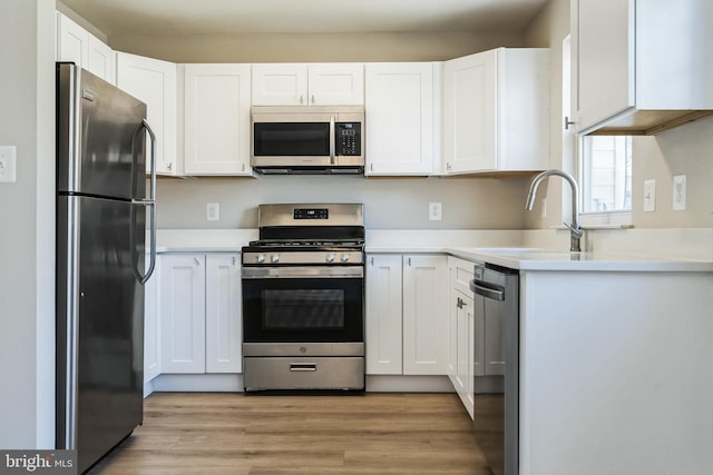 kitchen featuring light wood finished floors, white cabinets, appliances with stainless steel finishes, and a sink