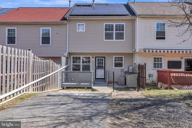 rear view of property featuring roof mounted solar panels, a fenced backyard, and a shingled roof