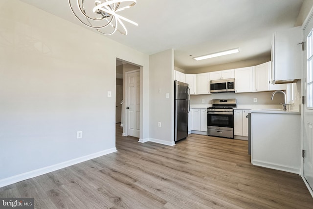 kitchen featuring light wood-style flooring, white cabinetry, stainless steel appliances, an inviting chandelier, and light countertops