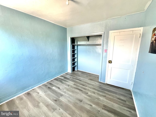 unfurnished bedroom featuring wood finished floors, a closet, a textured wall, and baseboards