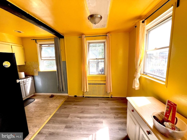 interior space with light wood finished floors, baseboards, radiator heating unit, freestanding refrigerator, and white cabinetry