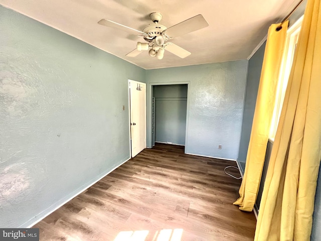 unfurnished bedroom with a ceiling fan, wood finished floors, a closet, baseboards, and a textured wall