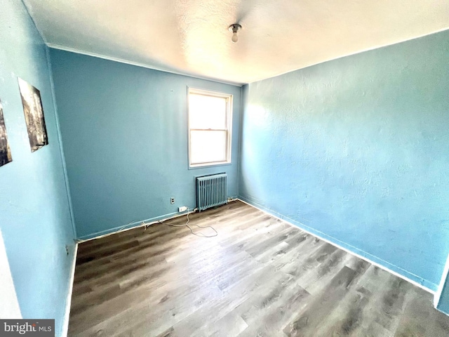 spare room with radiator heating unit and wood finished floors