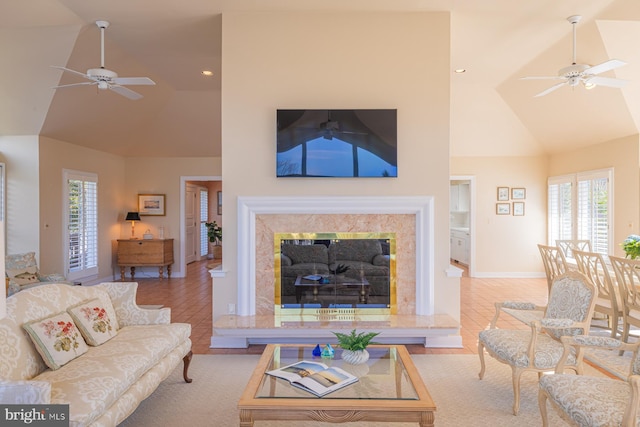 living area with ceiling fan, high vaulted ceiling, a healthy amount of sunlight, and a premium fireplace