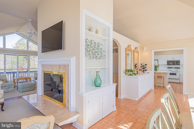 living room featuring high vaulted ceiling, a ceiling fan, a high end fireplace, arched walkways, and light tile patterned floors