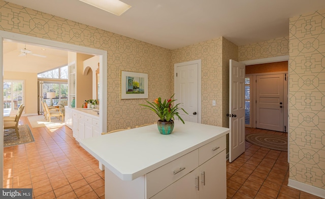 kitchen featuring wallpapered walls, baseboards, light countertops, light tile patterned flooring, and white cabinetry