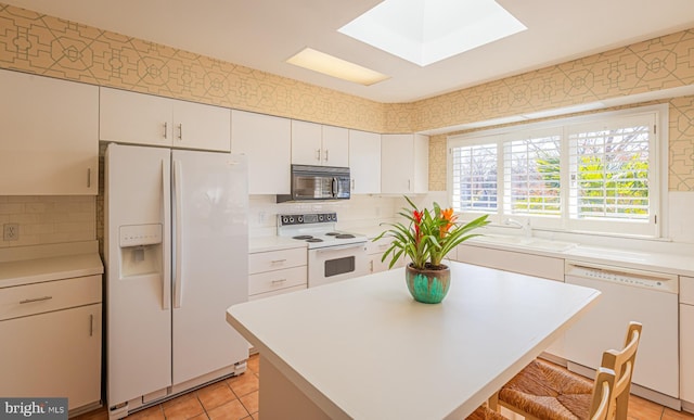 kitchen with white appliances, a skylight, light countertops, and a sink