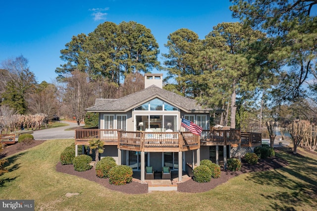 rear view of house with stucco siding, a lawn, a sunroom, and a wooden deck