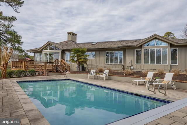 back of property with a deck, a patio, an outdoor pool, and board and batten siding