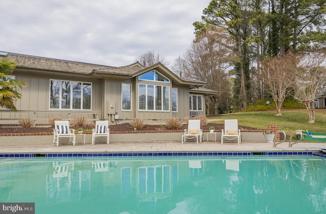 rear view of property with a yard, an outdoor pool, and board and batten siding