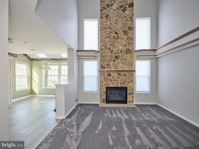 unfurnished living room with a stone fireplace, carpet, baseboards, and high vaulted ceiling