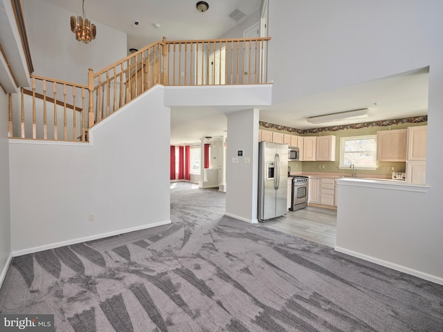 unfurnished living room with visible vents, baseboards, a sink, a towering ceiling, and light carpet