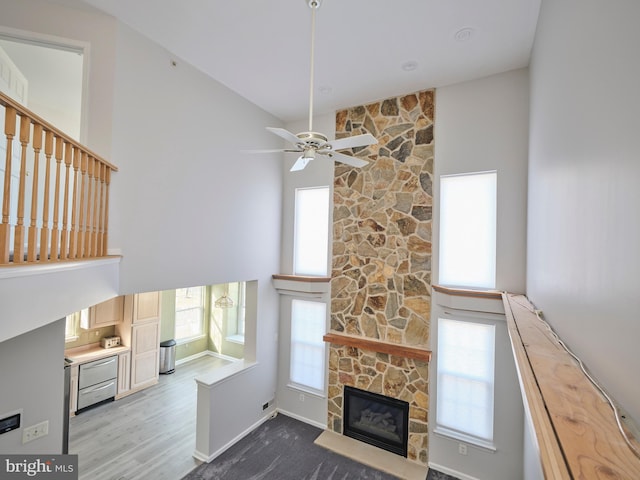 unfurnished living room featuring a stone fireplace, wood finished floors, a high ceiling, and a healthy amount of sunlight