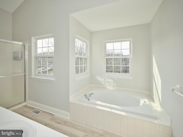 bathroom featuring wood finished floors, baseboards, visible vents, a shower stall, and a garden tub