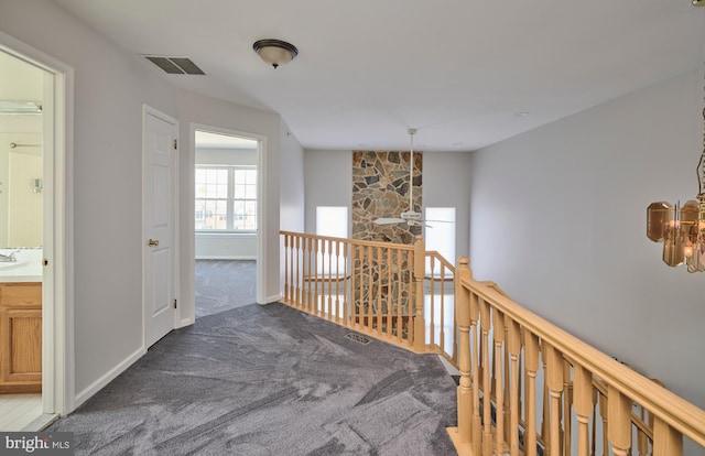 corridor with visible vents, an upstairs landing, baseboards, and carpet flooring