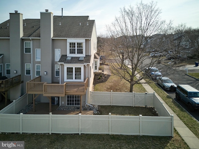 back of property with a fenced front yard, a shingled roof, and a gate