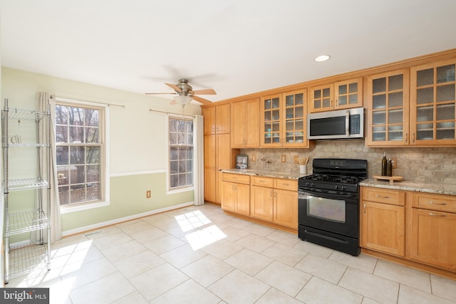 kitchen featuring stainless steel microwave, black range with gas stovetop, light stone countertops, and decorative backsplash