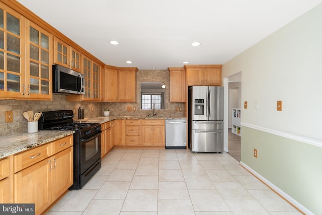 kitchen with a sink, backsplash, appliances with stainless steel finishes, light tile patterned floors, and light stone countertops