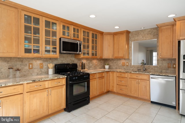 kitchen with a sink, backsplash, appliances with stainless steel finishes, glass insert cabinets, and light stone countertops