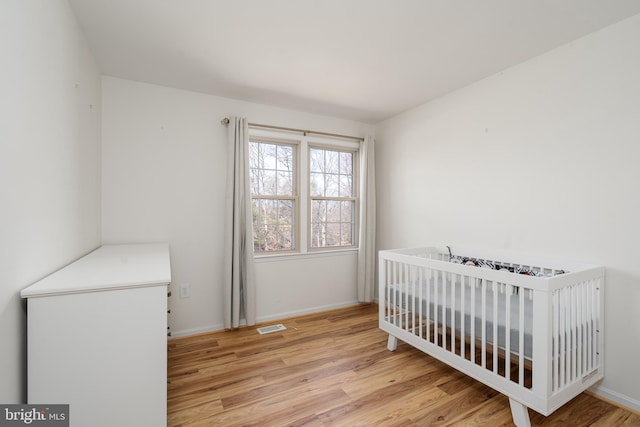 bedroom featuring visible vents, a nursery area, light wood-type flooring, and baseboards