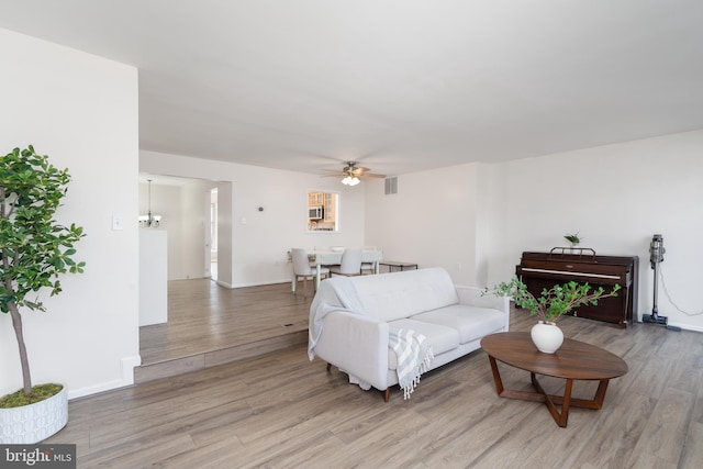 living room with visible vents, ceiling fan with notable chandelier, baseboards, and light wood-style floors