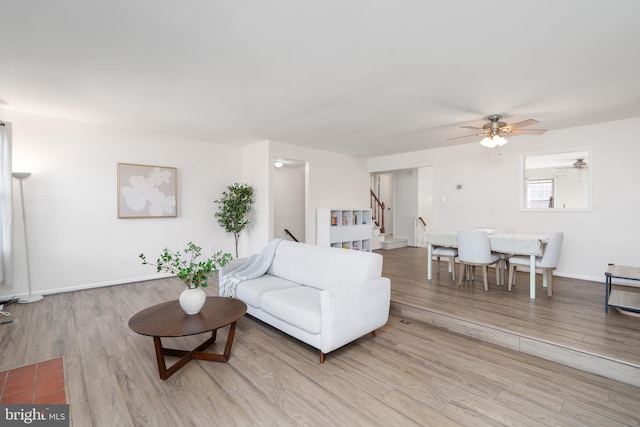 living room featuring ceiling fan, baseboards, wood finished floors, and stairs