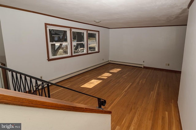 empty room featuring baseboards, baseboard heating, wood finished floors, and crown molding