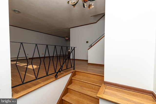 stairs with a notable chandelier, baseboard heating, and wood finished floors