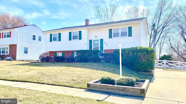 raised ranch with brick siding, a chimney, a front lawn, and fence