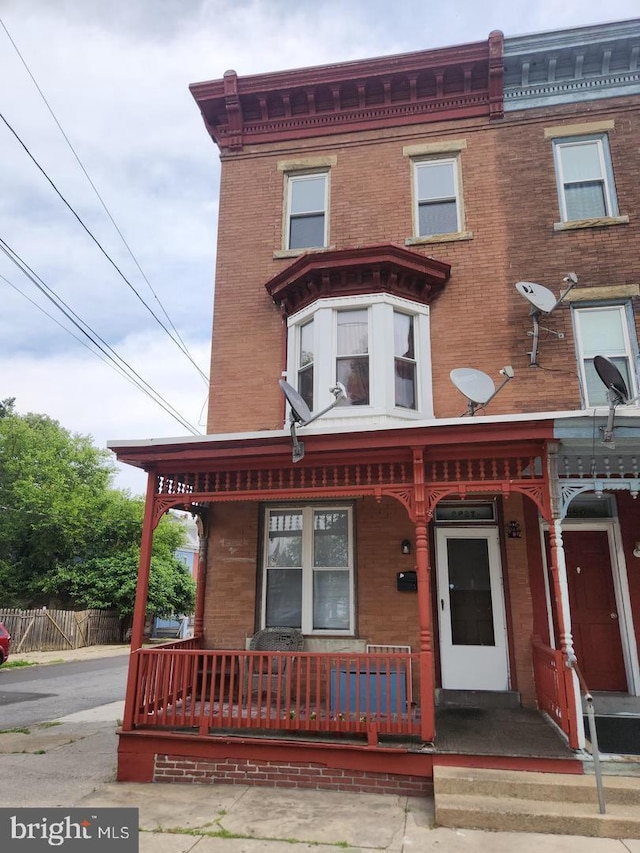 view of front of home with a porch, fence, and brick siding