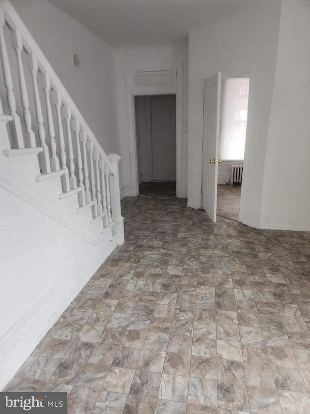 unfurnished room featuring stairs and radiator heating unit