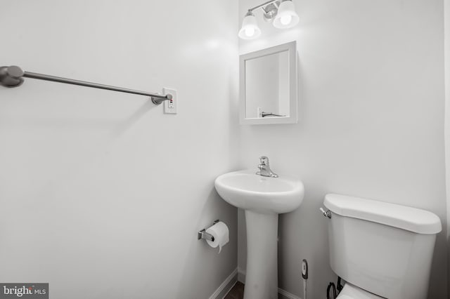 half bath with toilet, baseboards, and a sink