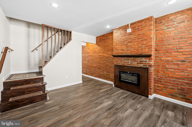 unfurnished living room featuring a glass covered fireplace, wood finished floors, baseboards, and brick wall