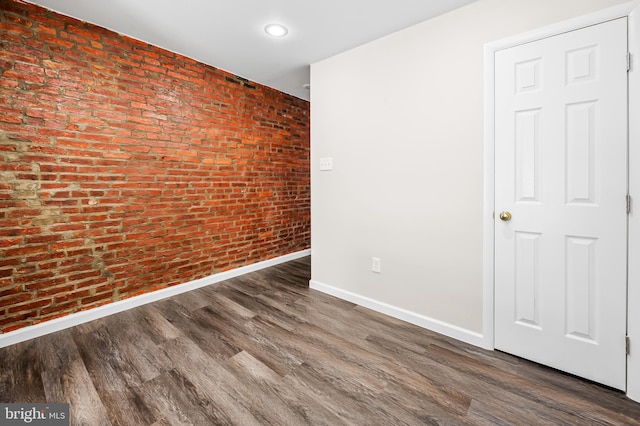 unfurnished room with brick wall, baseboards, and wood finished floors