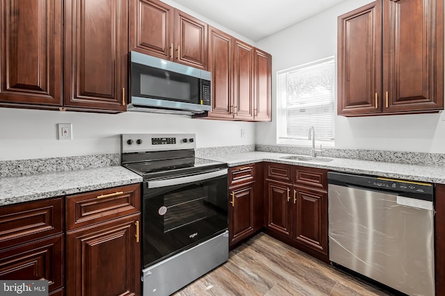 kitchen with light stone countertops, light wood-style floors, appliances with stainless steel finishes, and a sink