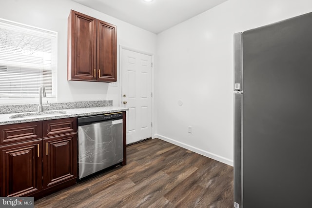 kitchen featuring baseboards, dark wood finished floors, light stone counters, stainless steel appliances, and a sink