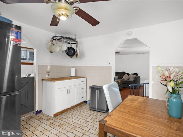 kitchen with wainscoting, freestanding refrigerator, arched walkways, white cabinets, and tile walls