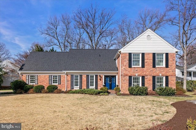 view of front of home featuring a front yard, brick siding, and roof with shingles