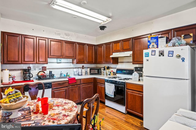 kitchen featuring range with gas stovetop, light wood-style flooring, freestanding refrigerator, under cabinet range hood, and black microwave