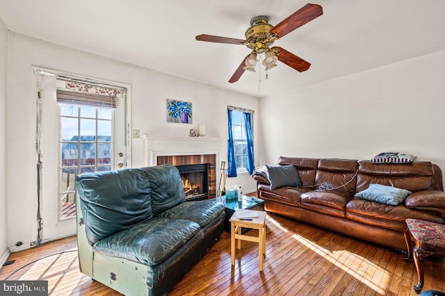 living room featuring light wood-style flooring, a fireplace, and a ceiling fan