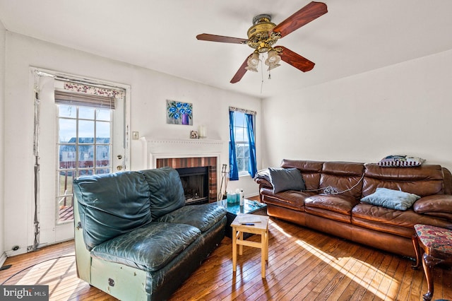 living area with light wood-type flooring, a brick fireplace, and ceiling fan