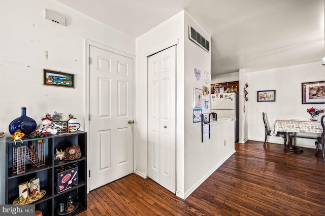 hall featuring dark wood-type flooring, baseboards, and visible vents