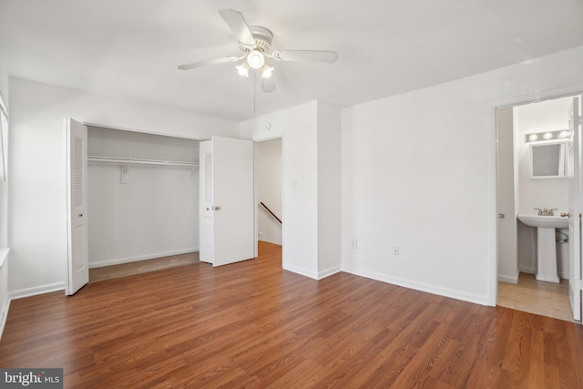 unfurnished bedroom with ensuite bath, wood finished floors, a closet, and baseboards