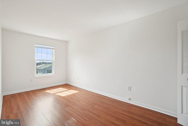 empty room featuring visible vents, wood finished floors, and baseboards