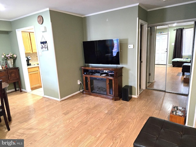 living room with a glass covered fireplace, baseboards, light wood finished floors, and ornamental molding