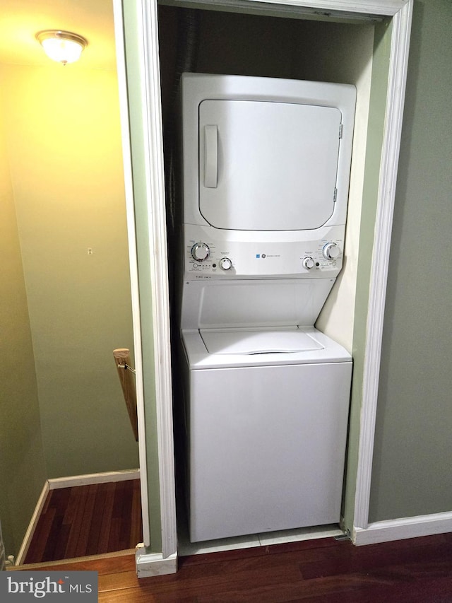 washroom featuring baseboards, wood finished floors, laundry area, and stacked washing maching and dryer