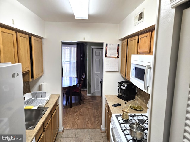 kitchen featuring white appliances, light countertops, brown cabinets, and a sink