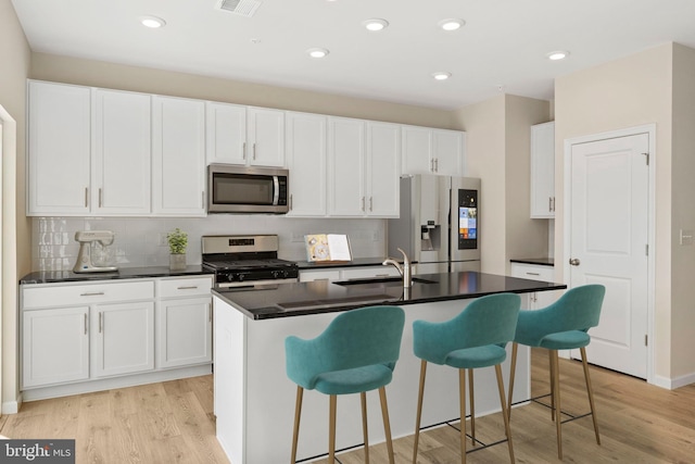 kitchen featuring dark countertops, a center island with sink, appliances with stainless steel finishes, and light wood-type flooring