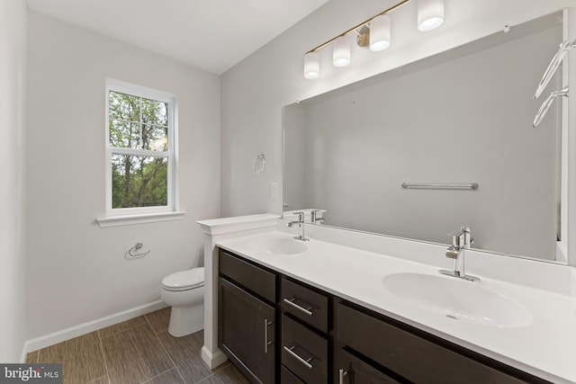 bathroom with a sink, baseboards, toilet, and double vanity